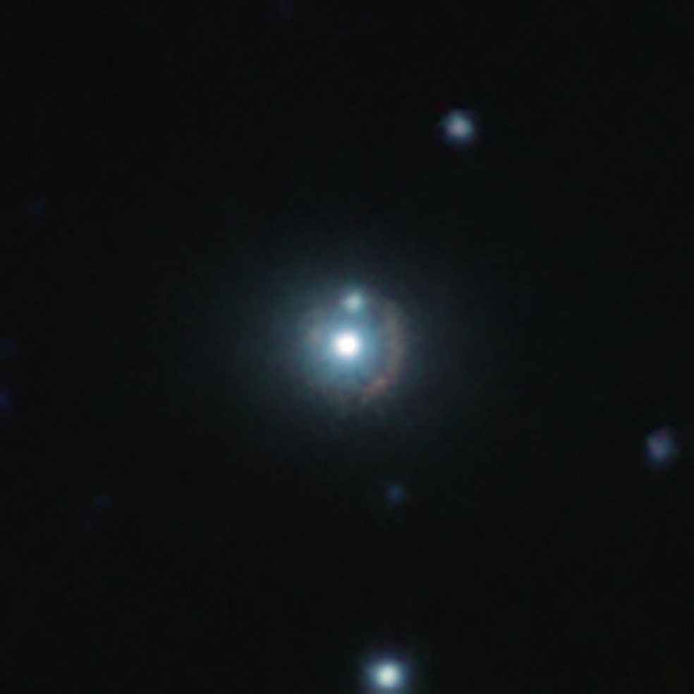 Visão infravermelha da galáxia distante 9io9, vista aqui como um arco avermelhado curvado em torno de uma galáxia próxima e brilhante — Foto: ESO/J. Geach et al.