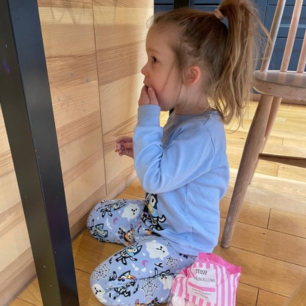 Juno Hersee-Hoicka, a filha de três anos do professor Hoicka, comendo marshmallows escondida debaixo da mesa da cozinha — Foto: Elena Hoicka