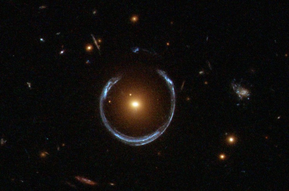A gravidade de uma galáxia vermelha luminosa (LRG) distorceu gravitacionalmente a luz de uma galáxia azul muito mais distante. Mais tipicamente, essa curvatura de luz resulta em duas imagens discerníveis da galáxia distante, mas aqui o alinhamento da lente é tão preciso que a galáxia de fundo é distorcida em uma ferradura, um anel quase completo. — Foto:  ESA/Hubble & NASA